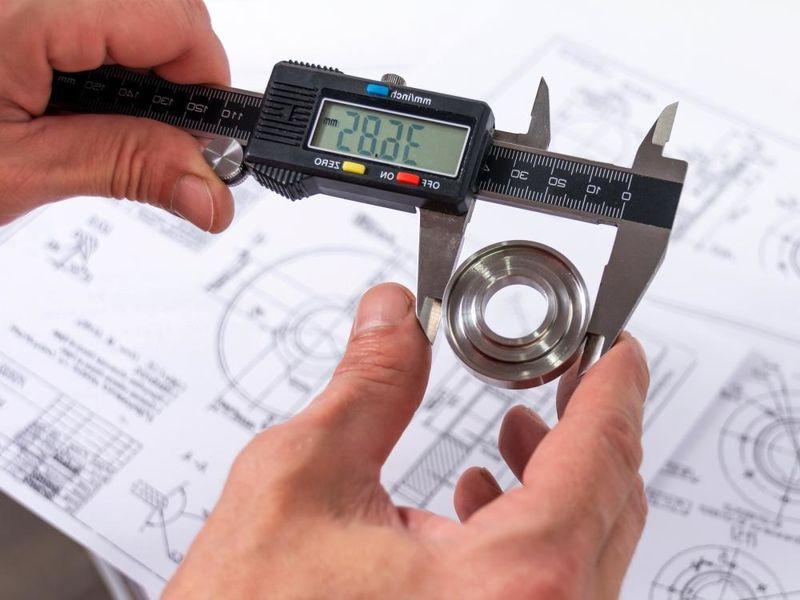 质量工程师用卡尺测量生产零件以确保其符合要求, 在后台有一个参考图.